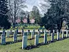 Rader av hvite gravsteiner står på en grønn gravlund omgitt av trær og vårblomstring.